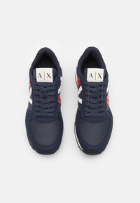 Merinau wornit avokadumalli, jossa on verkko ja mokka yläosa. Ominaisuudet ovat valkoisia ja punaisia korostuksia, litteät nauhat ja merkkilogo kielekkeessä.