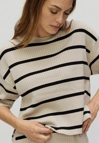 Beige ribbad stickad topp med horisontella svarta ränder, rund halsringning och korta ärmar med en avslappnad passform.