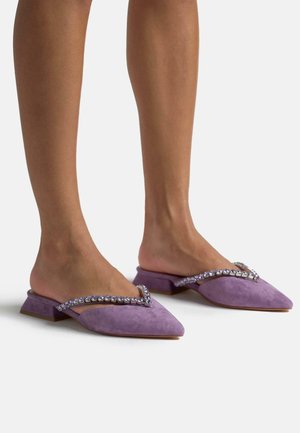 Mules en suède violet avec un bout pointu, un petit talon carré et une sangle ornée de pierres précieuses violettes le long du bord supérieur.