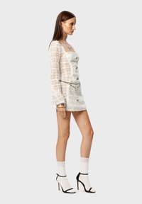 Weißes, strukturiertes Minikleid mit quadratischem Ausschnitt, langen Ärmeln und Knopfdetails, kombiniert mit Schwarz-weißen Absatzsandalen und Socken.
