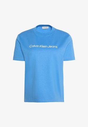 Světle modré tričko s krátkým rukávem a kulatým výstřihem s bílým nápisem "Calvin Klein Jeans" přes prsa.