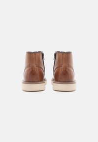 Botas de tobillo de cuero marrón con un acabado suave, que cuentan con una cremallera lateral y una suela de goma beige. Detalles de costura sutiles realzan el diseño.