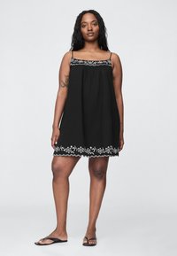 Črna obleka brez rokavov z vezenim belim cvetličnim vzorcem vzdolž roba. Iz lahkega blaga, z ohlapnim krojem in tankimi naramnicami.