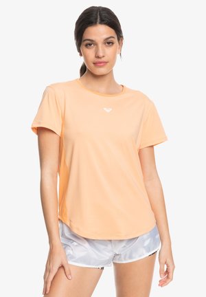 Peach-colored athletic t-shirt with short sleeves, round neckline, and a small white logo on the chest, worn with light gray shorts.