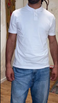 Homme portant un polo blanc uni à manches courtes et un jean bleu, debout à l'intérieur contre un mur texturé avec des décorations.