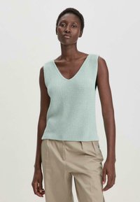 Lichtgroene mouwloze gebreide top met een V-hals, ribbelstructuur en een rechte zoom, gecombineerd met beige broek.