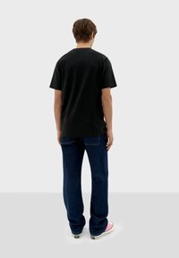 Camiseta negra de manga corta, de material de algodón, con un corte relajado, combinada con jeans azul oscuro y zapatillas blancas con acentos en rosa.