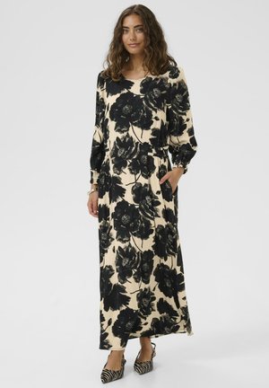 Długa, kwiecista sukienka w odcieniach czerni i kremu, z bufiastymi rękawami, elastycznym pasem i bocznymi kieszeniami. Nosi ją w połączeniu z paskowanymi szpilkami.