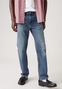 Jeans de mezclilla de lavado claro con corte recto. Presentan un desvanecimiento sutil, diseño clásico de cinco bolsillos y una cinturilla estándar. Combinados con zapatos negros.