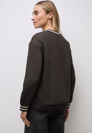 Tmavě hnědý crewneck svetr s ribovanými manžetami, který má bílé a černé pruhy. Hladký povrch a uvolněný střih, viditelný zadní pohled.