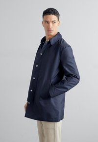 Marineblaue, wasserfeste Trenchcoat mit einem Knopfverschluss, zwei Seitentaschen und einem flachen Kragen. Hergestellt aus leichtem, glattem Material.