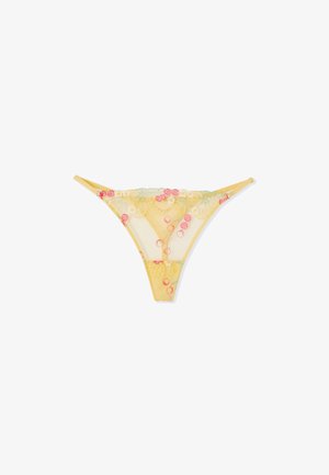 String en dentelle jaune transparente avec broderie florale en rose, blanc et vert, avec fines bretelles latérales sur fond blanc.