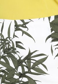 T-shirt i bomull med en gul sektion och en vit botten prydd med gröna bladtryck; mjuk textur och avslappnad design.