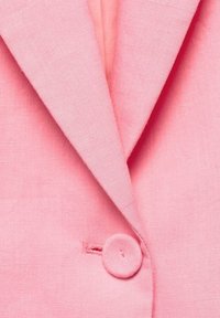 Gros plan sur le revers d'un blazer rose et un bouton assorti recouvert de tissu, fermant le devant.