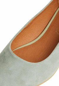 Světle zelená semišová slip-on obuv s texturovaným svrškem, kulatou špičkou a koženou stélkou v odstínu tan, s nízkým profilem.