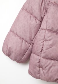 Chaqueta acolchada de color rosa claro con un sutil patrón de leopardo, que presenta secciones acolchadas y mangas redondeadas para calidez y comodidad.