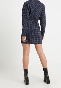 Marinblå rutklänning med långa ärmar och figursydd silhuett, i en texturerad tyg och med en bakre knytdetalj; matchad med svarta klackboots med blockklack.