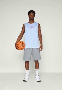 Camisola atlética sem mangas de cor azul clara com logótipo rosa, calções cinzentos, ténis brancos e uma bola de basquetebol, em segundo plano neutro.