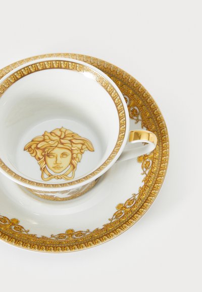 Porcelænskop og underkop med gulddetaljer, der prydes af et medusahoved. Komplekse blomster- og geometriske mønstre pryder underkoppens kant.