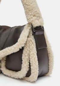 Borsa di pelle marrone con tracolla in shearling beige soffice, caratterizzata da una forma rettangolare e una texture liscia. Include un dettaglio con clip metallica.