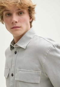 Graues, geripptes Hemd mit Knopfleiste und Kragen, mit zwei Brusttaschen und schwarzen Knöpfen. Der Stoff hat ein strukturiertes, weiches Aussehen.