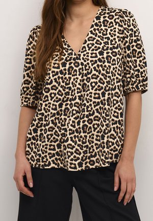 Kobieta nosząca luźną bluzkę w panterkę z pufiastymi krótkimi rękawami i dekoltem w kształcie litery V, połączoną z czarnymi spodniami.