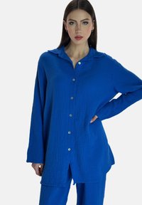 Camisa de botones azul hecha de tela texturizada con cuello, con botones en la parte delantera y mangas largas. Combinada con pantalones azules a juego.