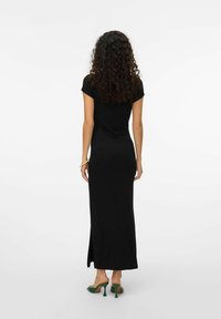 Czarna maxi sukienka z krótkimi rękawami, dopasowanym krojem i bocznym rozcięciem. Modelka ma na sobie zielone szpilki. Gładki materiał i minimalistyczny design.