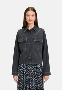 Czarna kurtka dżinsowa z dwoma przednimi kieszeniami, srebrnymi ćwiekami na kieszeniach i lekko skróconym krojem. Zestawiona z wzorzystą spódnicą.