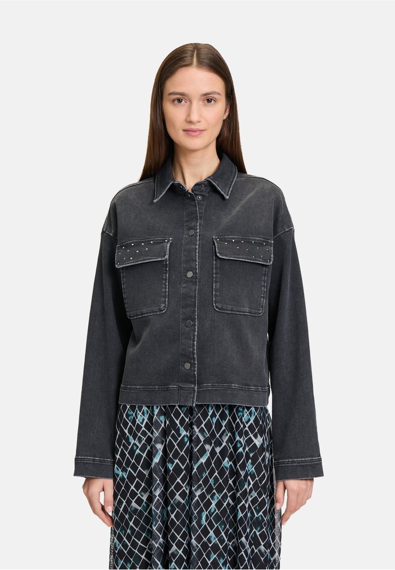 Czarna kurtka dżinsowa z dwoma przednimi kieszeniami, srebrnymi ćwiekami na kieszeniach i lekko skróconym krojem. Zestawiona z wzorzystą spódnicą.