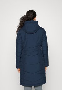 Tmavě modrý prošívaný kabát s kapucí, má vzor prošívání ve tvaru šipky a elastické manžety. Látka působí hladce a je voděodolná.