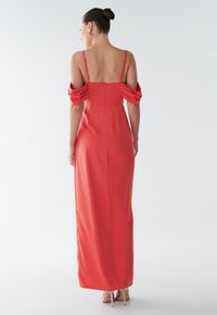 Lång, figursydd klänning i korallfärgat tyg med axelbandslösa puffärmar och dragkedja baktill. Slät textur och ankellång.