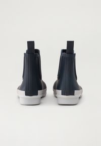 Marineblaue Gummistiefel mit gewellter Textur, grauer Laufsohle und Zuglaschen. Die Rückansicht hebt die Ferse und Konstruktionsdetails hervor.