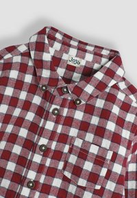Camicia di flanella a quadri rossi e bianchi con colletto a punta, bottoni a pressione in metallo e taschino sul petto; il tessuto presenta una trama a zig-zag.