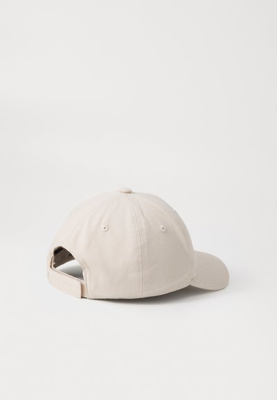 Gorra de béisbol de algodón beige con visera curva, correa ajustable en la parte posterior y ojales de ventilación. Tela texturizada, construcción de seis paneles.