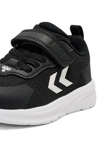 Zwarte sportieve schoen met een bovenwerk van mesh, voorzien van een zwarte klittenbandsluiting, witte accenten en een gestructureerde rubberen zool.