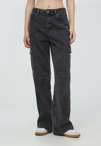 Czarne dżinsowe spodnie cargo o luźnym kroju, szerokich nogawkach, podwójnych bocznych kieszeniach oraz kontrastowym przeszyciu, z zapięciem na guzik i zamek błyskawiczny.