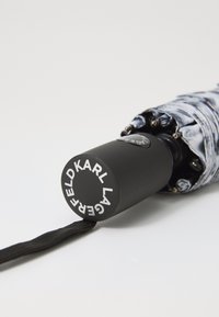 Black handle umbrella with a patterned fabric canopy, featuring a round button mechanism and a black strap for grip. Logo on the handle.