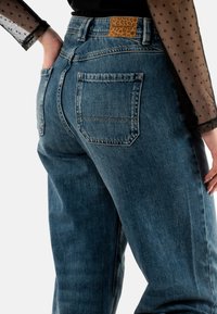 Jeans de mezclilla azul de cintura alta con un parche texturizado de leopardo marrón en la parte posterior de la cinturilla y dos bolsillos traseros.