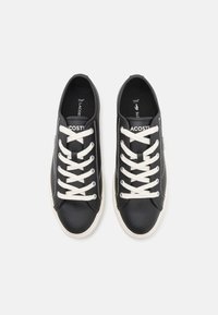 Sapatilhas de pele preta com atacadores brancos, apresentando um design de cano baixo, costuras em contraste e um logótipo na língua. A sola é de cor creme.