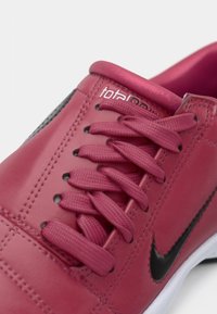 Rozā ādas sporta apavi ar noapaļotu purngalu, melniem akcentiem un teksturētām šņorēm. Iekļauj mīkstinātu apkaklīti un šūtus dekorus augšdaļā.