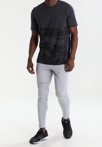 Camiseta con patrón de camuflaje gris y una superposición sólida, combinada con pantalones jogger ajustados de color gris claro y zapatillas deportivas negras.