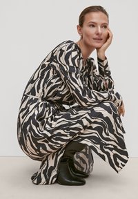 Langärmliges Kleid in Creme mit schwarzen Zebra-Streifen, seidiger Textur, knielangem Schnitt und seitlichen Schlitzen, kombiniert mit schwarzen Stiefeln.