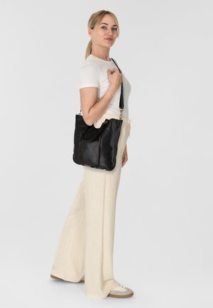 Sac à main en cuir noir avec un design décontracté, doté d'une poche avant et de clous décoratifs en métal. Bretelle ajustable incluse.