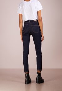 Jeans de tiro alto de color azul oscuro con corte ajustado y bolsillos traseros, combinados con una camiseta blanca y botas de tobillo negras con tachuelas.