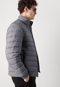 Lightweight, gray puffer jacket with horizontal stitching, high collar, and zip closure. Features elastic cuffs and side pockets.