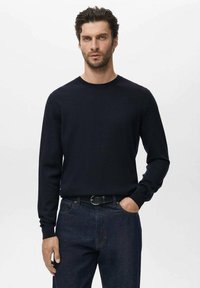 Suéter de manga larga azul marino en material suave, con cuello redondo, puños acanalados, combinado con jeans de mezclilla oscuros y un cinturón negro.