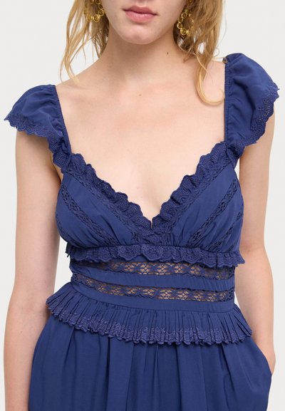 Navyblaues Kleid mit Rüschensäumen, Spitzenakzenten und einem gefalteten Saum. V-Ausschnitt mit horizontalem Spitzenpaneel.