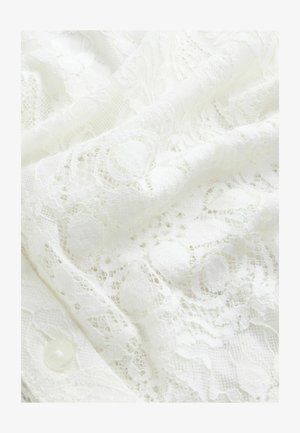 Hvid blonderstof med indviklede blomsterdekorationer, en blanding af teksturer og en glat overflade med en synlig knapdetalje.