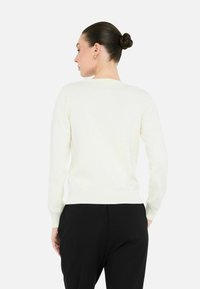 Kreemikasvärvi sviiter, kerge kudumisega, keha lähedal pikkade varrukatega, ümmarguse kaeluse ja soonikuga hemiga, koos mustade pükstega. Lihtne ja minimalistlik disain.
